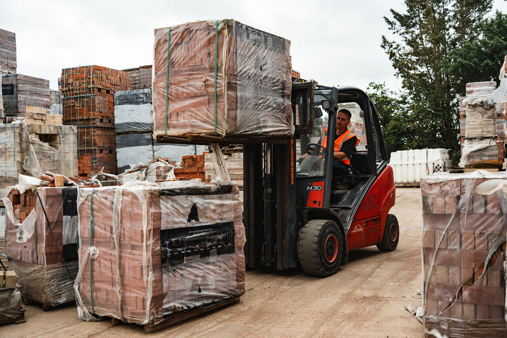 Forklift carrying a pack of bricks across the yard